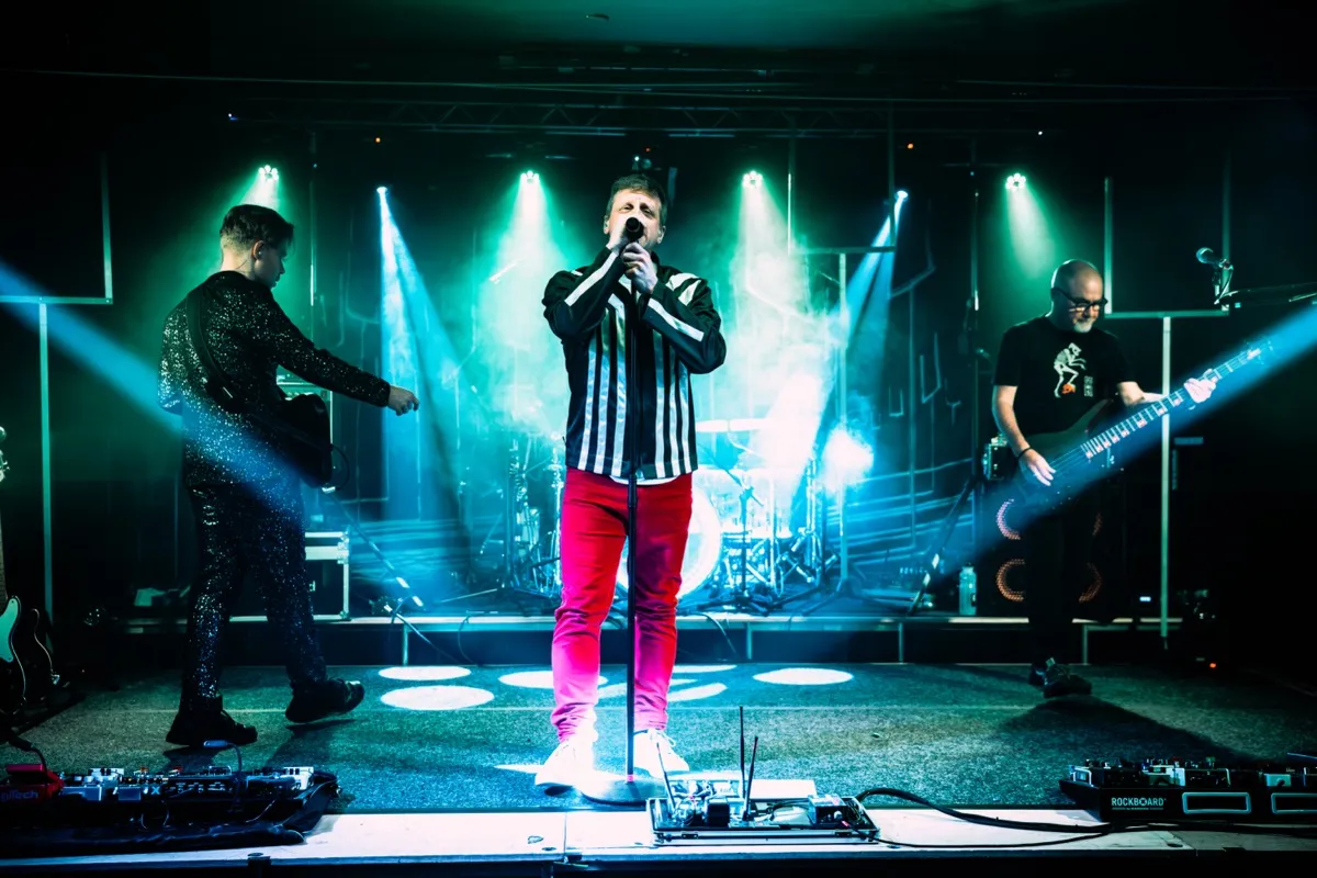 Full band performing with dramatic green and teal stage lighting